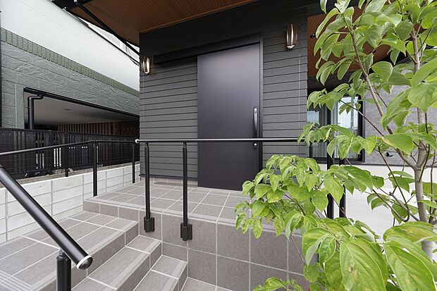 【5号地モデルハウス】アプローチに手摺を備えた安全設計で、その手前には外壁に映える鮮やかな植栽を設けています。