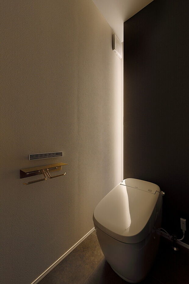【ホテルライクな家-トイレ】間接照明として取り入れた縦のラインの奥にはトイレットペーパーや小物が隠せる収納も。すっきりと生活感を無くしつつ日々の暮らしには役立つ収納も確保したハイブリッドタイプのレイアウト。