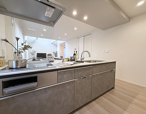 【F棟キッチン】リビングダイニングと繋がる開放感の高い対面型キッチン。家族のコミュニケーションはもちろん、IHクッキングヒーターやタッチレス水栓などの機能性とデザインが備わったキッチンです。