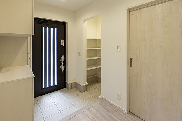 【【1階玄関/B号地】】玄関ドアはガラス入りデザイン。やわらかな自然光をエントランスへ導きます。雨具やベビーカーなどのお出掛け用品をまとめて保管ができる土間収納は扉を設けず、靴のままでスムーズに出入りいただけます。