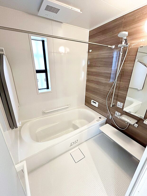 【浴室】清潔感あるホワイトを基調とした空間に、木目調のダークブラウンの壁面をアクセントに。温かみが感じられ、ほっとできる色合いは、のんびりくつろぐ浴室にぴったりです。（1号棟）
