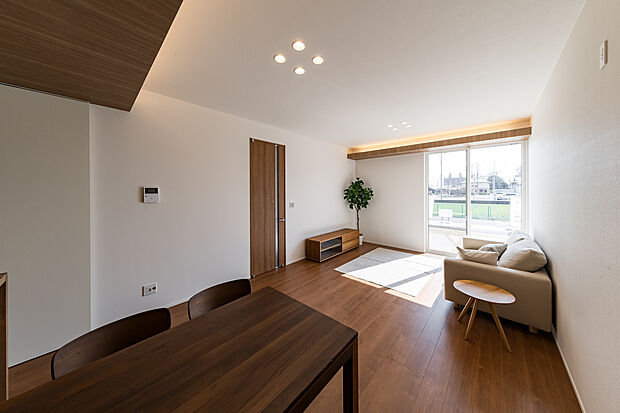 【Ｄ棟モデルハウス】広い庭とつながる大きな窓が、LDKに光と風を招き入れ、下がり天井と高い天井が立体的な奥行きを描く。間接照明とダウンライトが陰影を整え、家族が自然と集まる“内と外がひとつになる”リビングをつくり出す。