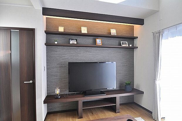 【リビング】TVボードを設置し、上部にはライトアップされた2段の飾り棚を配置。写真や雑貨を美しく演出でき、上質なリビング空間を彩ります。