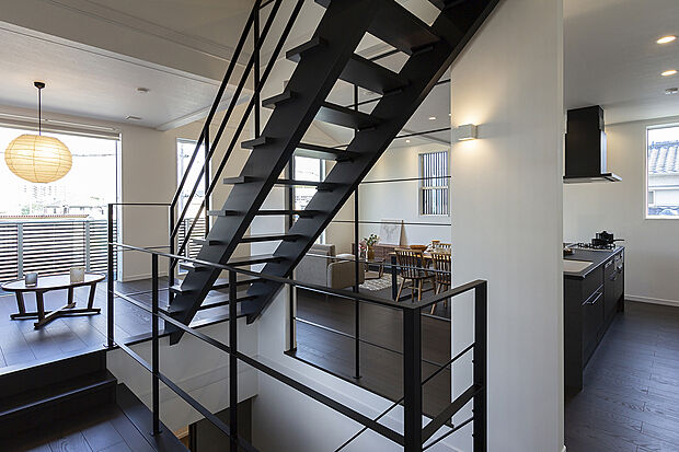 【【2階約17.5帖LDK/A号地モデルハウス】】細身のブラックの金属手すりや桁などにより、高いデザイン性が目をひくオープン階段。1階～上部ロフトまでを視覚的に連続してつなぎ、心地よい開放感や明るさを添えています。