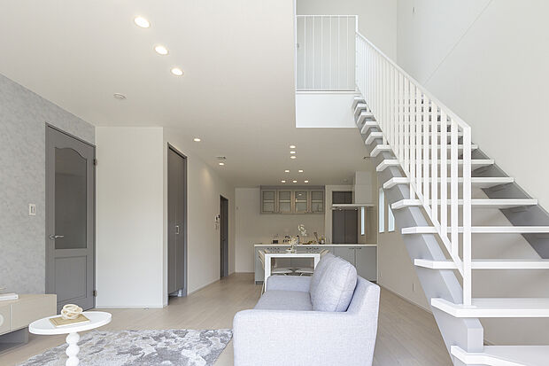 【【1階約18帖LDK/A号地モデルハウス】】ダウンライトにより空間の広がりを感じられ、吹抜に設けられたオープン階段を通して、上階からも自然光が降り注ぎます。階段手すりや踏み板はホワイトに。洗練された印象のリビング空間に溶け込みます。