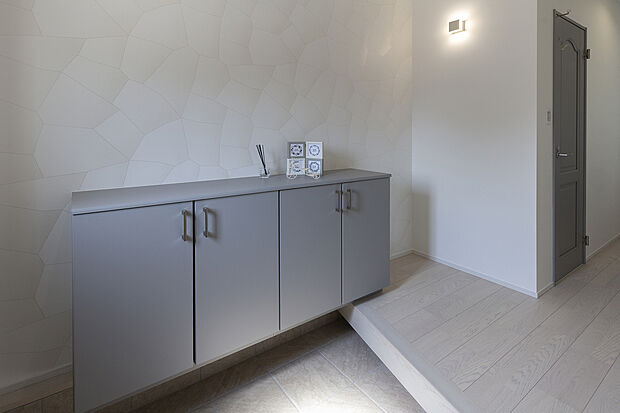 【【1階玄関/A号地モデルハウス】】斜め框やフロートタイプの玄関収納により奥行きを感じられ、クロスの質感や照明にもこだわりのホテルライクなエントランス。。土間収納を別に設けており、ベビーカーなどのかさばるお出掛け用品もキレイに収まります。