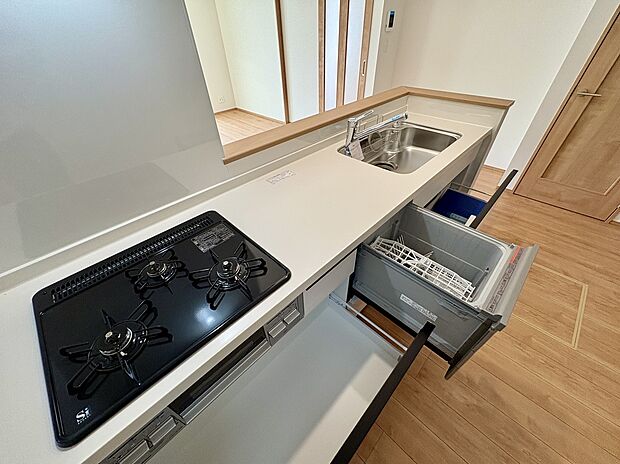 【【B号棟/キッチン】】広々としており、使い勝手良好なシステムキッチン。三口コンロが搭載されており、同時調理も捗ります。食器洗乾燥機付きで、洗い物の時短も叶いそうです。