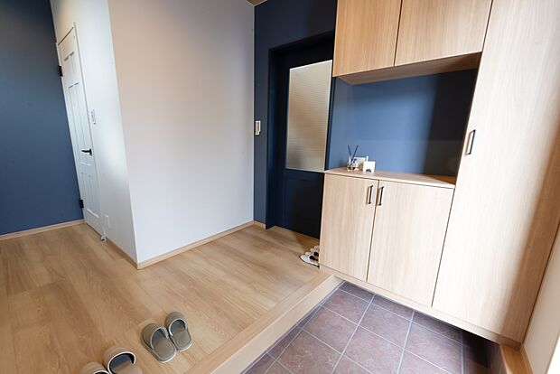 【1階玄関/A号地モデルハウス】広さを重視した設計のエントランス。土間収納を備え、履物のほか、濡れや汚れが気になるアイテムの収納に便利です。リビングドアは大きなガラスが光を通す、引戸を採用しています。