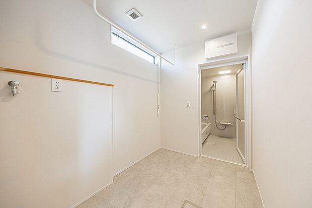 【4号棟】広いランドリールーム兼、脱衣室から繋がるバスルーム。季節や時間帯を問わず、またゲストに見られずに洗濯物を干せます。物干しの下に、収納を置ける充分なスペースがあります。