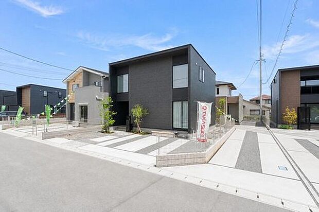 【6号地：緑が彩るゆとりのアプローチ】シンボルツリーが外観に温かみをプラス。前面の道幅も広く見通しが良いので、ベビーカーでのお出かけや毎日の車の出し入れもスムーズで安心です。
