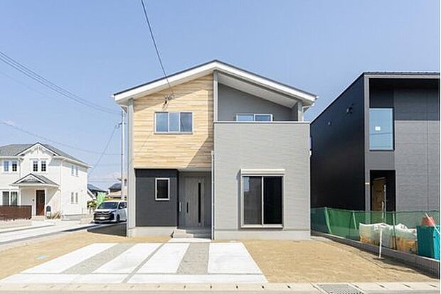【 現地外観写真】【7号地：個性が光るアシンメトリーな屋根の外観】明るい木目調とグレーを組み合わせた、カフェのようにナチュラルで可愛らしい佇まい。斜めにカットされた特徴的な屋根が、デザイン性をぐっと高めています。