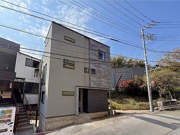 【現地外観写真】グレーと石目調の外壁が調和する、洗練されたモダンな邸宅。プライバシーに配慮した窓配置と、表情豊かなデザインが目を引きます。落ち着きある住環境で、自分らしい上質な暮らしを叶えます。