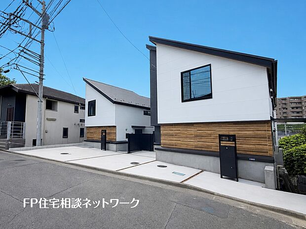 【現地外観写真】【外観】 白の外壁に木目調のアクセントが映えるモダンな外観。複数台駐車が可能なゆとりあるカースペースを完備しています。洗練された新邸で、心地よい新生活を。