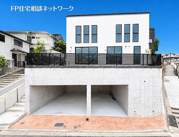 【現地外観写真】青空に映えるホワイトの外観と、重厚感のあるコンクリートのビルトインガレージのコントラストが印象的な住まい。2階部分には開放的なバルコニーも完備されており、都会的な暮らしを叶えます。