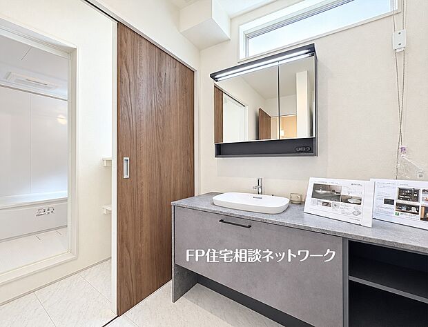 【洗面台・洗面所】【洗面脱衣室】  幅が広く使いやすい洗面化粧台を備えた洗面脱衣スペースです。グレーの天板がお洒落で、鏡の裏や下部には収納スペースも充実。引き戸を採用しており、限られた空間でもスムーズに出入り可能です。