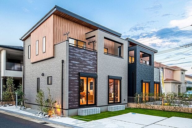 【 住協建設の施工例 】異素材が織りなす洗練のファサード。 温もりのある木目パネルとグレーのコントラスト。開放的なテラスが暮らしに彩りを添えるデザイン住宅。
