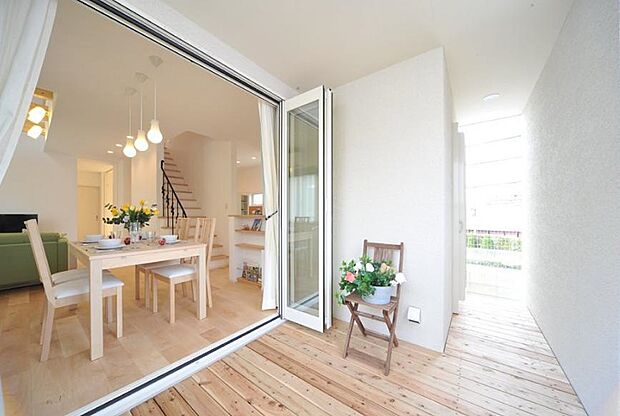 【建物プラン例（内観写真）】視線が通るようレイアウトされた、広々開放的なリビングと屋根のあるデッキテラス。吹き抜けから差込む柔らかな光と優しい色使いの内装は、明るく落ち着いた印象。階段を中心に8の字に回れる回遊動線で使いやすいです。晴れの休日にはセカンドダイニングまでまでテーブルを延ばして、カフェ気分を味わったりと思い思いに過ごせます。/当社施工例