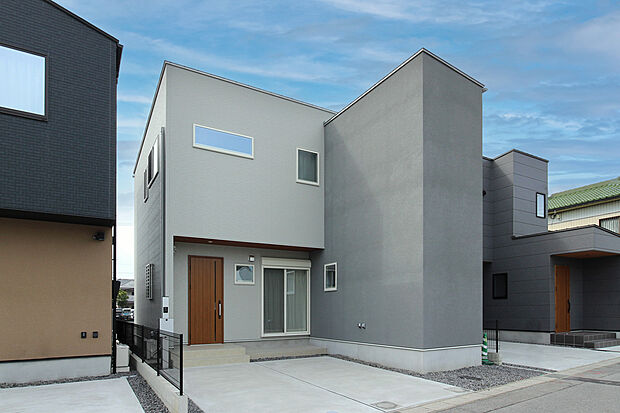 B棟｜ホワイトのサイディングを基調に、グレーの塗り壁（ジョリパット）をアクセントとして採用。 玄関ドアと軒天には木目を取り入れ、シンプルながら温かみのある外観に仕上げました。