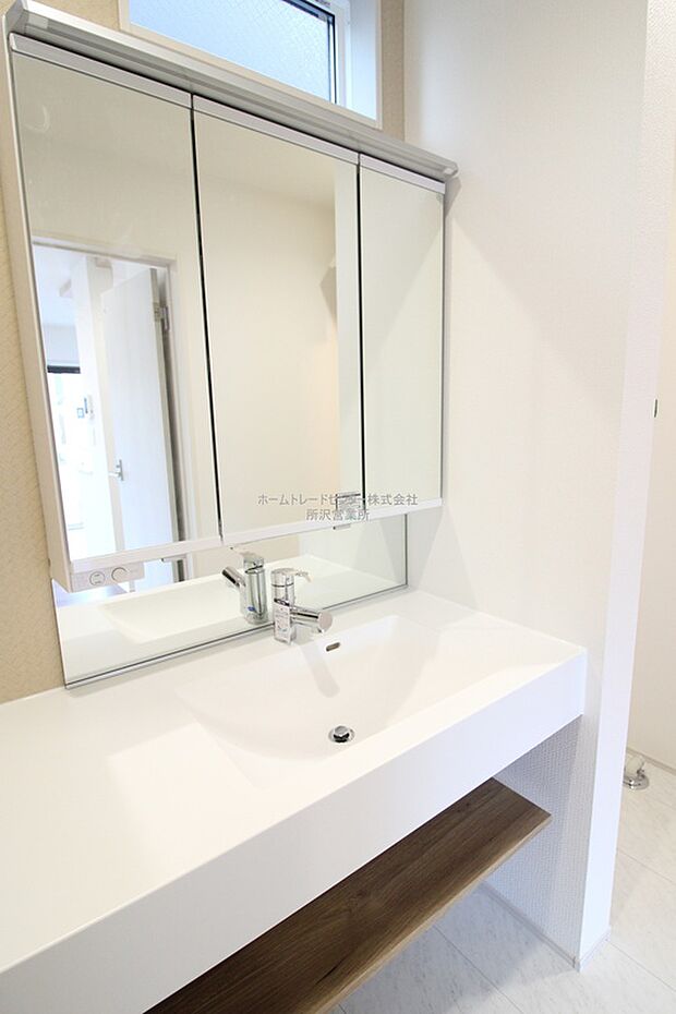 【洗面所】ワイドタイプの化粧台は、扉を付けない宙に浮かせたスタイル。石目や木調の落ち着いたテイストを組み合わせ、洗練された印象です。フルフラットのカウンターはお掃除ラクラク。デザインと機能性を両立しました。