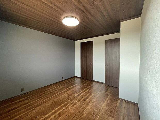 【主寝室】天井の木目調クロスとグレーのアクセント壁が、まるでホテルのような上質な安らぎを演出。ゆとりある8.5畳の広さに加え、大型のウォークインクローゼットも完備しており、心も荷物もスッキリ整う主寝室です。