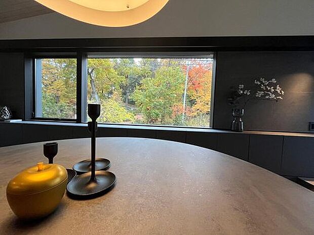 ダークトーンのモダンな内装と、窓の外に広がる鮮やかな紅葉のコントラストが印象的です。曲線的な照明とシックな小物が、落ち着きと上質さを感じさせます。