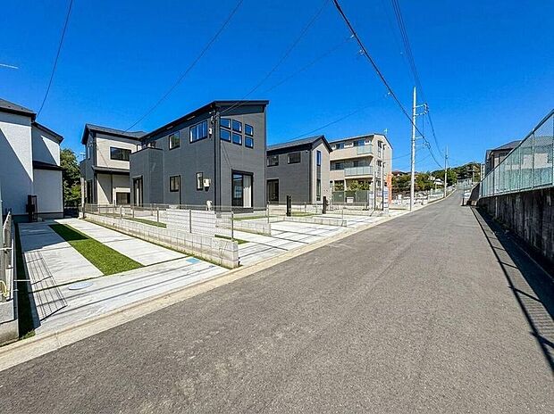 【前面道路含む現地写真】青空が広がる開放的な新築分譲地。統一感のあるモダンな外観と、各戸にゆとりの駐車スペースを確保。新しい家族の暮らしがここから始まります。