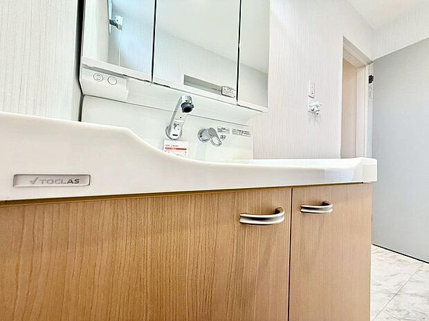 【洗面所】ボウル一体型カウンターと三面鏡収納を備えた洗面台。木目調のやさしいデザインが朝に安らぎを添え、明るく清潔感のある空間で気持ちよく一日をスタート。