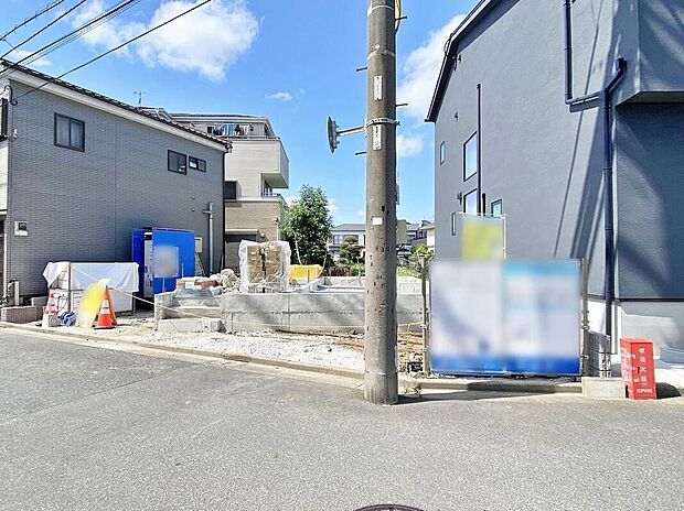 【現地外観写真】現地(2026年8月)撮影
基礎工事中の敷地と両隣の建物が写っています。前面はアスファルト舗装の公道で電柱が敷地前に立っています。土地約102.84m2、木造2階建て予定。