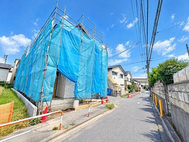 【前面道路含む現地写真】青い養生シートで覆われた建築中の外観写真。アスファルト舗装の公道（幅約4～5.4m）に面する住宅地で、木造2階建・駐車1台、完成予定は2026年11月です。現地（2026年10月）撮影