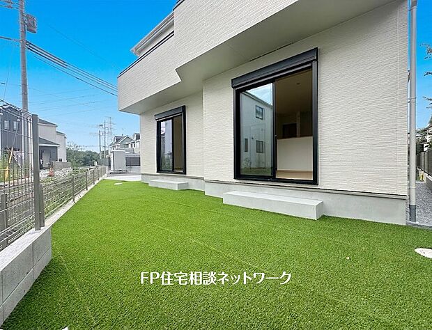 【庭】住宅の掃き出し窓から続く、緑色の人工芝が敷かれた庭。2カ所の窓の前にはコンクリート製のステップが設置され、庭への出入りが可能。隣地との境界にはメッシュフェンスが設置されている。
