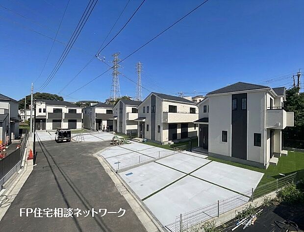 【前面道路含む現地写真】複数の新築一戸建て住宅が並ぶ分譲地。全棟にコンクリート舗装された広い駐車スペースが確保され、一部には人工芝も敷かれている。
