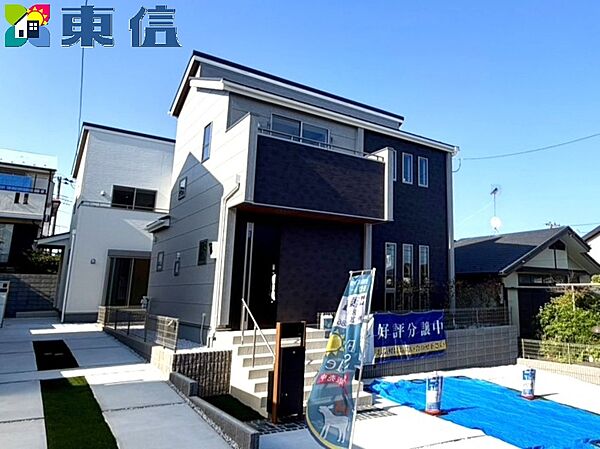 1号棟外観　青い空に映えるスタイリッシュな外観！シックな黒のアクセント壁と洗練されたグレーのコントラストが際立つ新築戸建てです。明るい陽射しが差し込む開放的な佇まいで、毎日の暮らしを贅沢に彩ります。