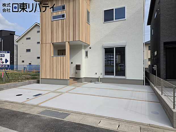 【並列2台駐車の外観写真】木目と白の外壁を配した2階建て外観。並列2台分のコンクリート駐車スペース