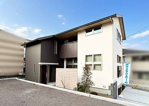 【13号棟】コントラストの強いツートンカラーと、奥行きのある形状が、角度によって様々な表情を見せる外観です。深く取られた軒天とバルコニーの木目が、自然な温かみとアクセントを加えています。