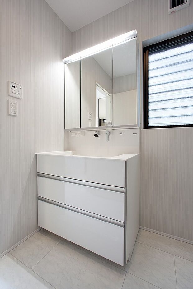 【洗面台】【2号地同仕様写真】
白を基調としたストライプ柄の壁紙が、洗練された印象を与える洗面所。明るい窓から光が差し込み、毎日の身支度を心地よく演出。高機能な設備で快適な暮らしを。