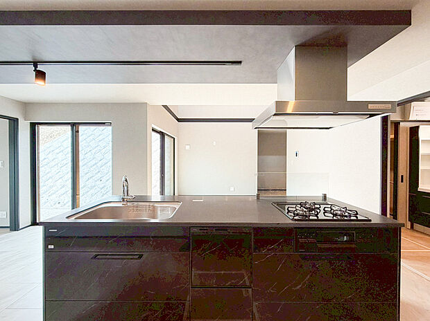 洗練されたブラックの石目調デザインが目を引く、ワイドなアイランドキッチンです。キッチン上部にはダクトレール照明と下がり天井を配し、まるで高級レストランのようなモダンな空間を演出しています。