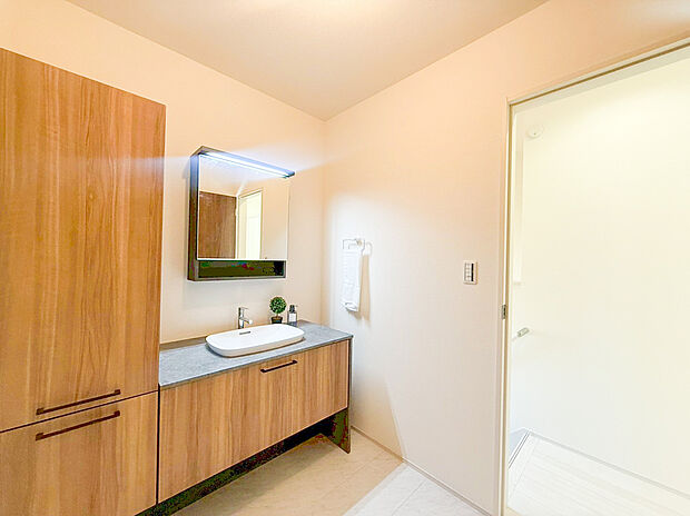 【洗面化粧台】木目調の扉と、スタイリッシュなグレーのカウンターが調和した洗練されたデザインの洗面化粧台です。ベッセル式の洗面ボウルがホテルのような上質な空間を演出し、毎朝の身支度を贅沢なひとときに変えてくれます。