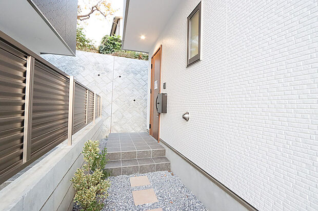 【隣接住戸との関係に配慮した玄関アプローチ 2号棟】家の顔となる玄関は、格調高いデザイン性が求められます。玄関は、高級感と断熱性、防犯性に優れた玄関ドアを標準装備。デザイン性だけではなく、ピッキング対策に優れたセキュリティサムターン等、防犯対策を考慮。