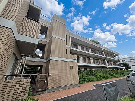 共用部側から見上げると、3階建ての建物形状や開放廊下の配置がよく分かります。敷地内には植栽が設けられ、住戸へと続く動線も確保されています。低層ならではの落ち着いたスケール感が感じられるマンションです。