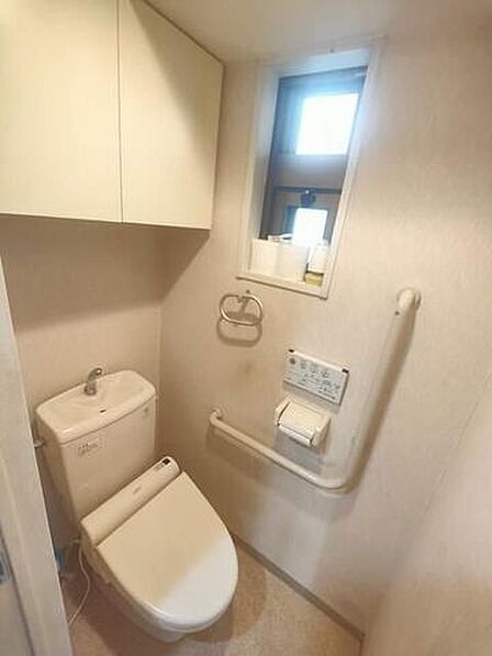 手洗い付きタンクや温水洗浄便座を備えたトイレには、立ち座りをサポートする手すりや小窓が設置されており、上部にはペーパー類などの保管に便利な作り付けの収納棚を備えています。