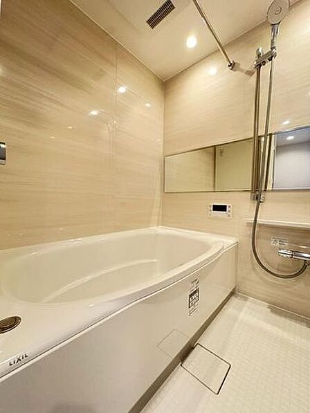 木目調の壁パネルが採用された浴室には、横長のワイドミラーや高さ調節が可能なスライドバー付きシャワーのほか、衣類乾燥や部屋干しにも活用できるランドリーパイプが設置されています。