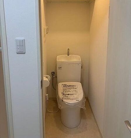 手洗い付きタンクが備え付けられた洋式トイレには、側面にペーパーホルダーやタオル掛けが配置されており、上部にはストック品などの整理に活用できる作り付けの棚が設置されています。