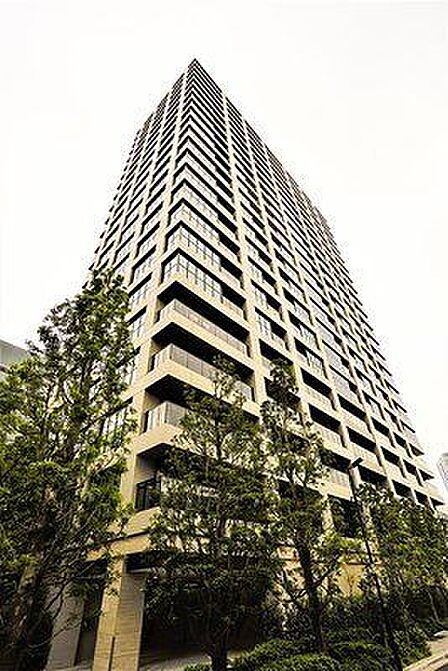 ベージュを基調とした落ち着いた色合いの外壁デザインが特徴的な高層マンションで、各階のバルコニーにはガラスパネルの手すりが採用されており、建物周辺には緑豊かな植栽がキレイに整えられています。