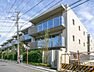 外観：ベージュを基調とした落ち着いたトーンの外壁に、ガラスパネルを採用したバルコニーが目を引く外観で、敷地周りには整えられた生け垣や植栽が配置されています。