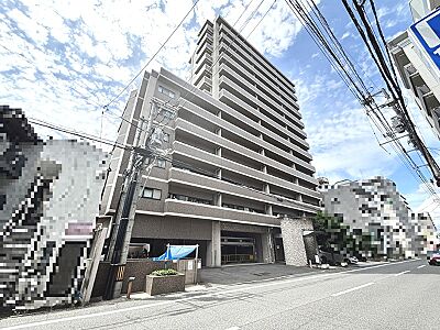 外観：存在感のある落ち着いた色合いのマンション。空を仰ぐようなアングルで、開放的な青空が広がります。