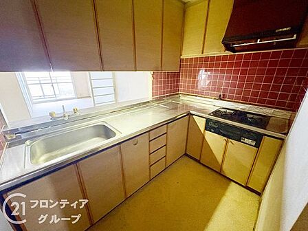 広々としたL字型キッチンは家事動線が良くお料理が捗ります 落ち着いた木目調のキャビネットと赤いタイルの壁が毎日のキッチンタイムに彩りと品格を添えてくれます