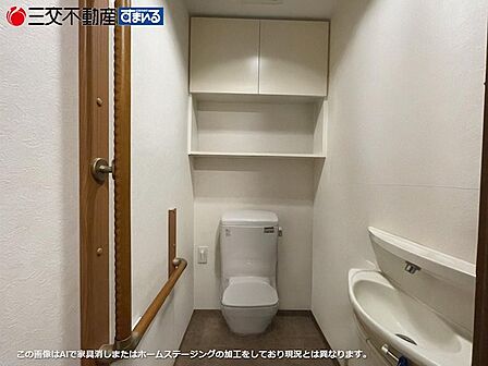 清潔感のある白い壁と機能的な収納棚が魅力のトイレ。独立した手洗い器と手すりも備え、快適な空間です。