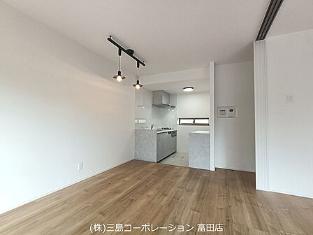 スタイリッシュなペンダントライトが空間を彩るリビング。明るい木目調のフローリングとホワイトの壁が、開放感のある印象を与えます。キッチンとの一体感で、家族との会話も弾みます。
