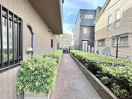 建物に挟まれた空間に緑の植栽が並び、落ち着いた佇まいを見せるアプローチです。
