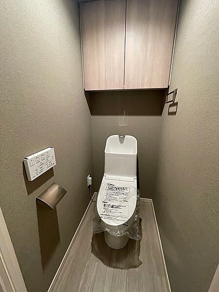 温水洗浄便座付きのトイレです。上部には収納棚があり、空間を有効活用できます。明るい色合いの床材が清潔感を演出します。